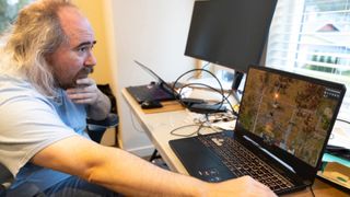 Tarn Adams sitting in front of a laptop, edited with a screen from Factorio