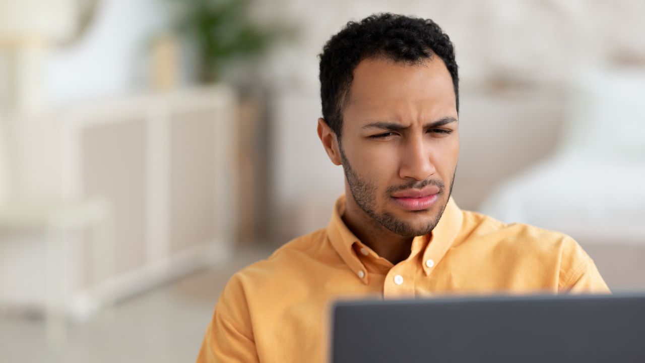 A man squints at his laptop, clearly needed eyeglasses.