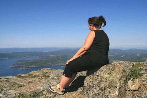 overweight woman sitting outdoors on a mountain overlooking water