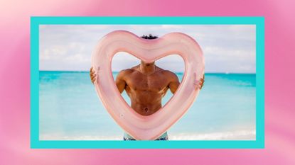 A male contestant from too hot to handle covering up his face with a heart pool float in front of a beach