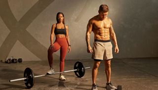 Man and woman in gym wear stand surrounded by weights
