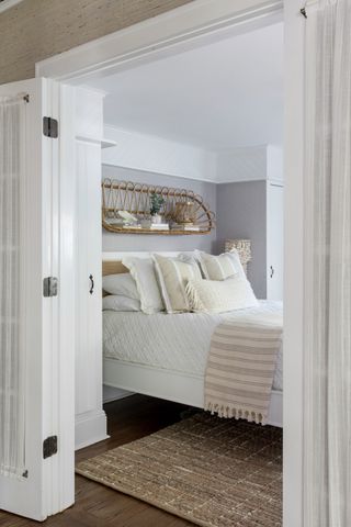 gray and white bedroom with rattan shelf above the bed, neutral textured bedding, wooden floor, rug