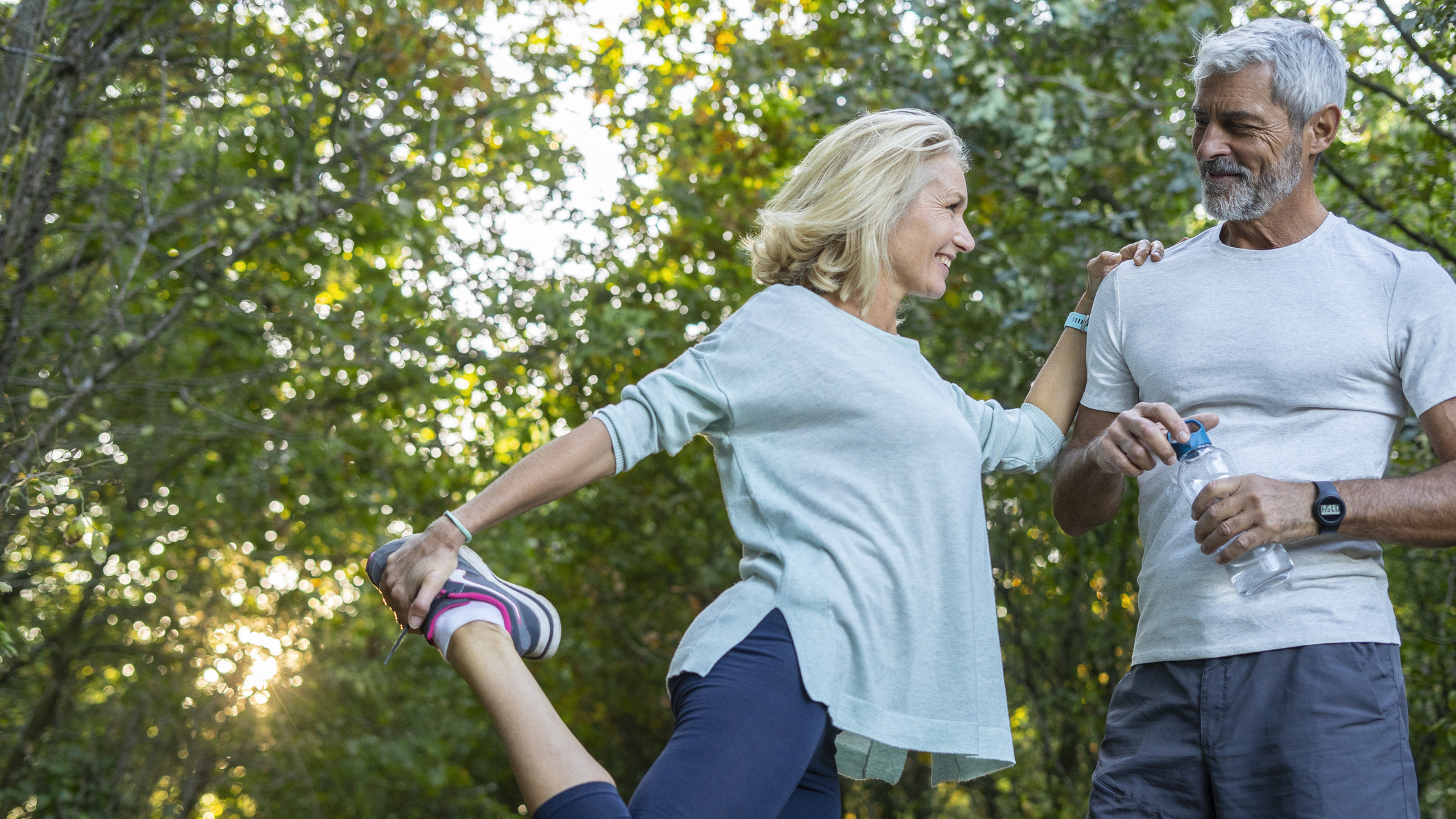 Woman holding her foot behind her with her knee bent, holding on to a man’s shoulder