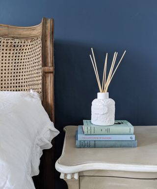 Scented diffuser on blue stacked books on bedside table.
