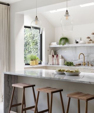 A brightly lit kitchen with white counters and wooden bar stools