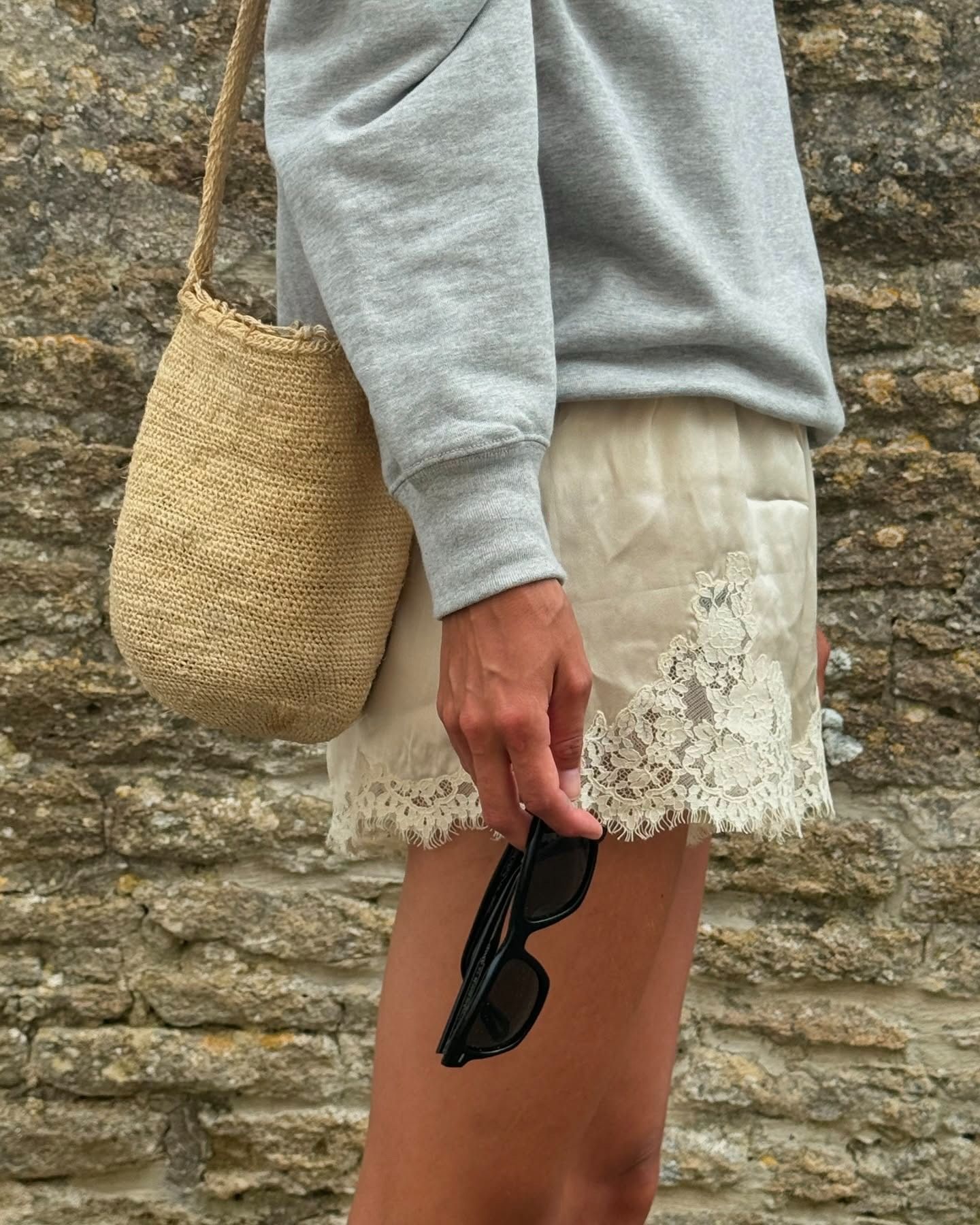 Laura Vidrequin wearing a gray sweatshirt with lace-trim Doen shorts and a raffia shoulder bag.