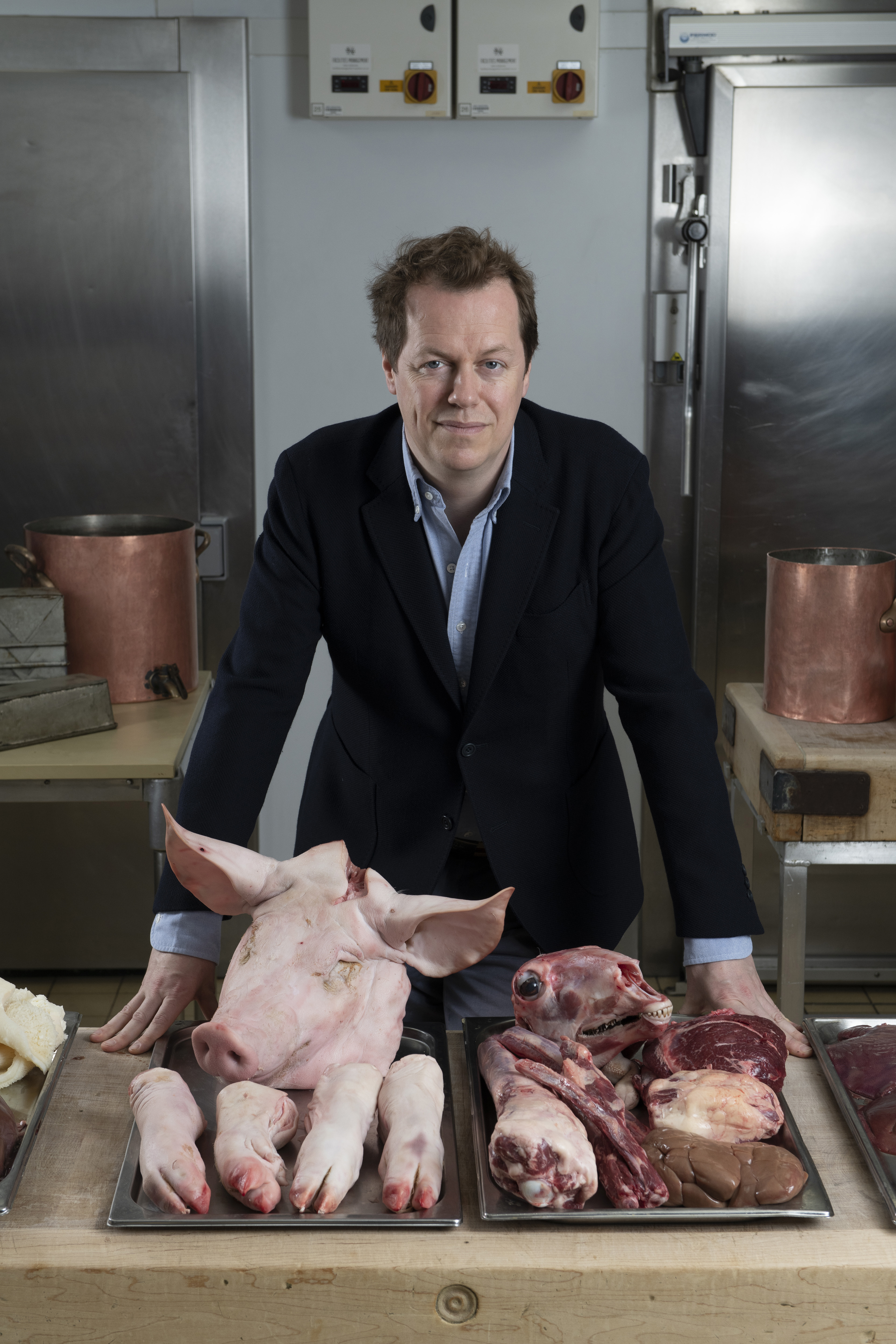 Tom Parker Bowles standing infront of two plates of raw offal including a pig&#039;s head