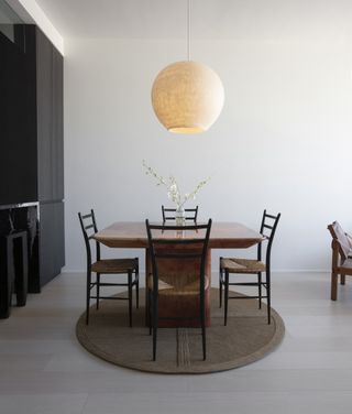A minimalist living room with a round wooden dining set and a globe lampshade