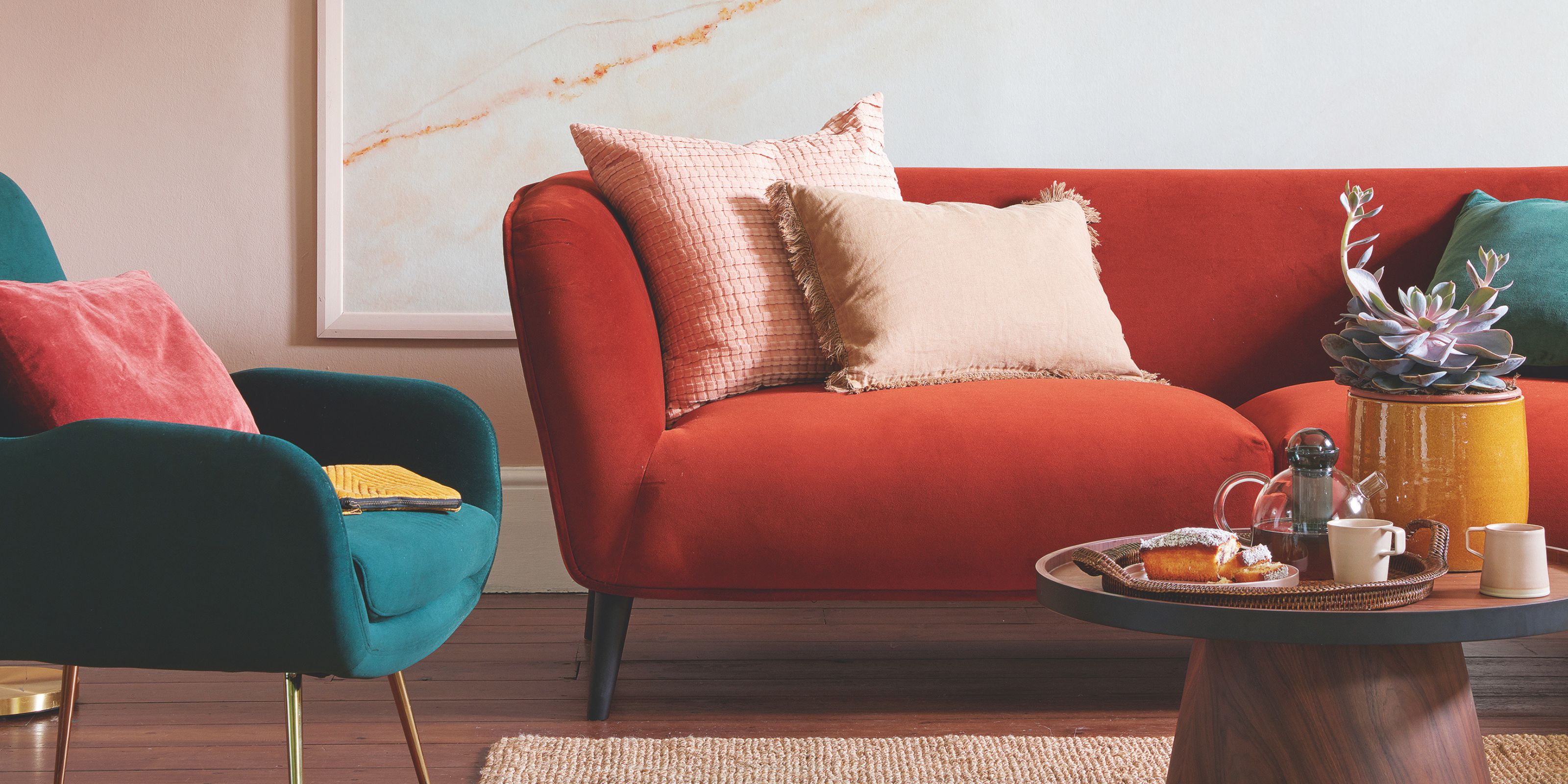 A dark wood floor and pink walled living room with two velvet plush sofas
