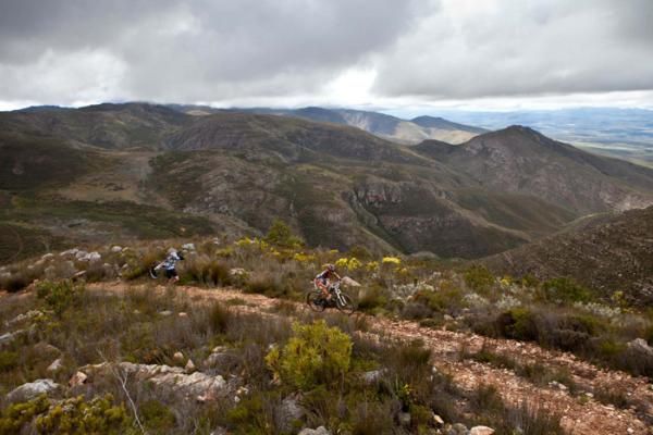 One rider pedals while another carries his bike up a stoney climb through the Kamanassie Mountains on stage 4