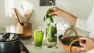 Woman's hand putting spinach into blender with milk to make smoothie