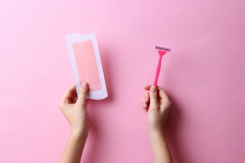 A person holding a razor and a wax strip.