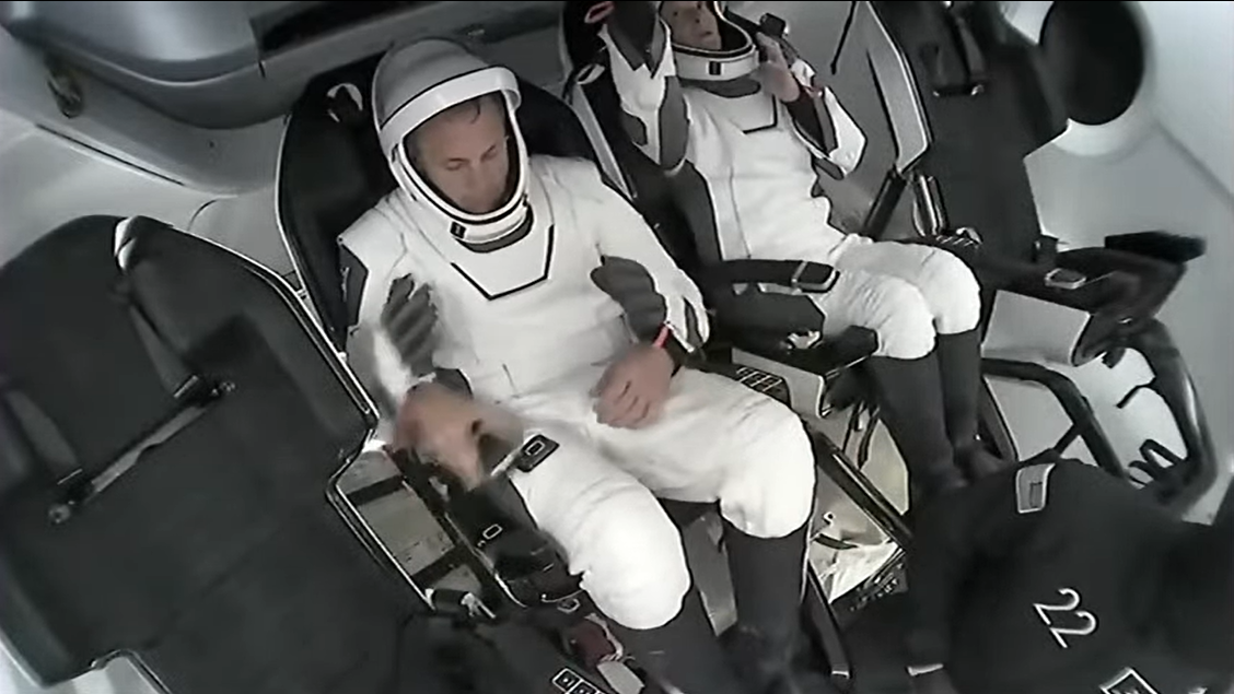 two people in white spacesuits in a row of spacecraft seats