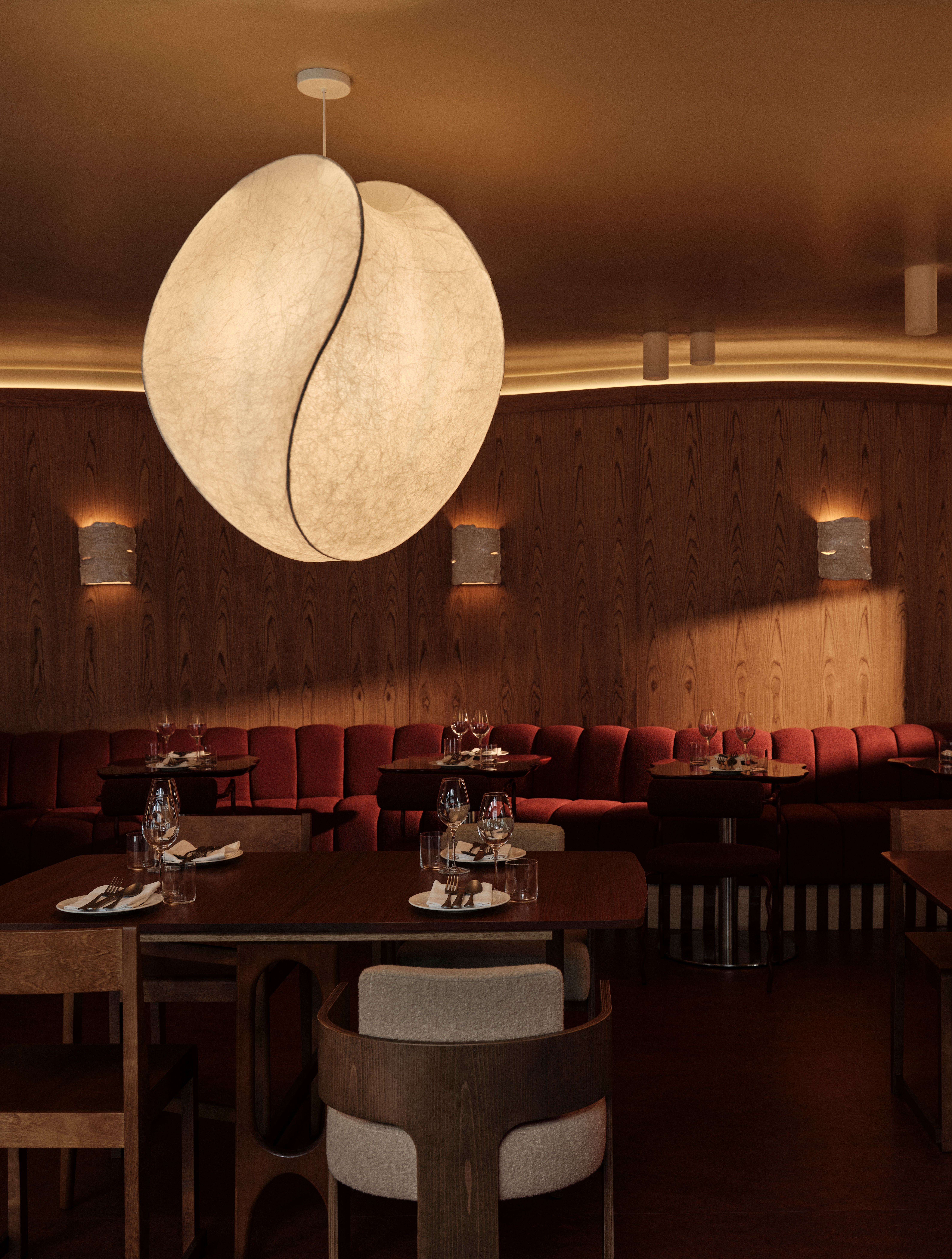 Interior shots of a restaurant decorated with soft wood walls, oversized modular couches in creamy shades, upholstered banquettes in bordeaux and brown shades, sculptural lighting, and a collection of records.