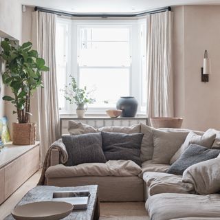 A neutral-coloured small living room with a corner sofa and matching floor-length curtains