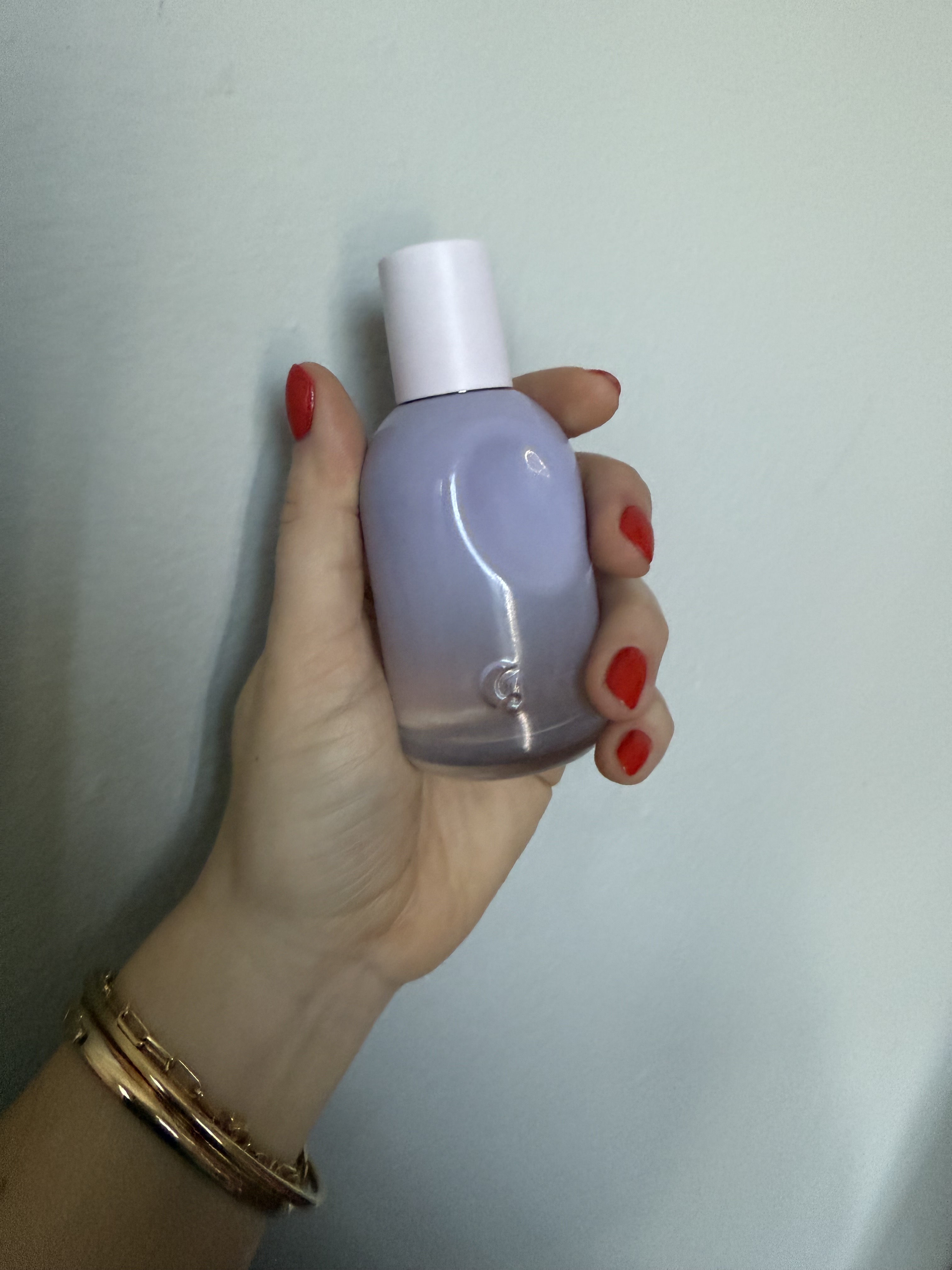 hand holding up glossier you fleur perfume bottle against grey wall