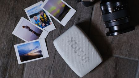 The Fujifilm Instax Mini Link 3 mobile photo printer on a gray background with instant photos