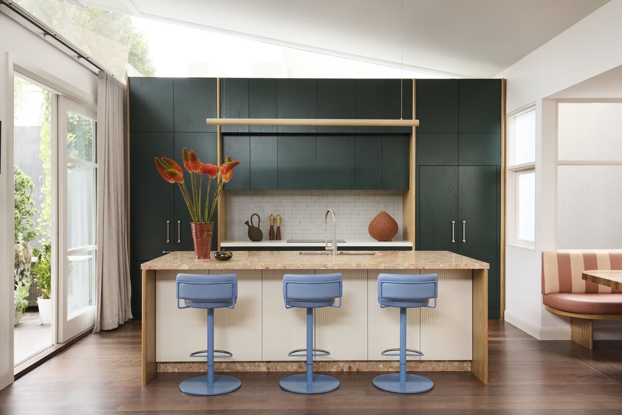 colorful kitchen with green cabinets, blue bar stools, orange marble, and vase of flowers