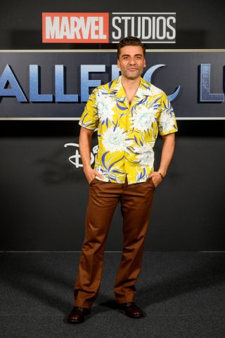 Oscar Isaac standing in a yellow Hawaiian shirt, with copper pants, at the Spain Moon Knight premiere.
