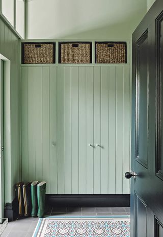 A mint green closet in a mudroom with storage above it