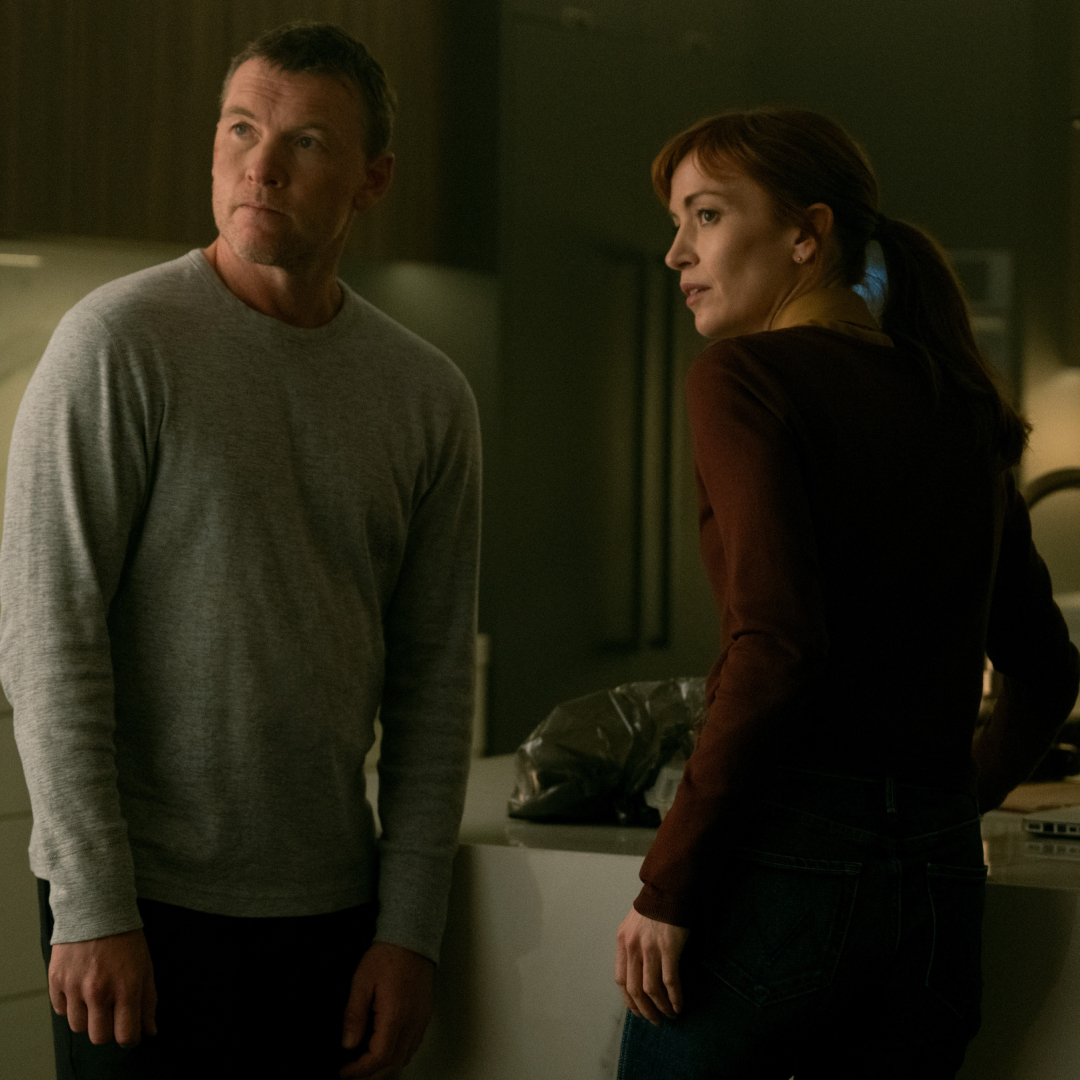 sam worthington as david and britt lower as rachel looking nervous over their shoulders in a kitchen in i will find you