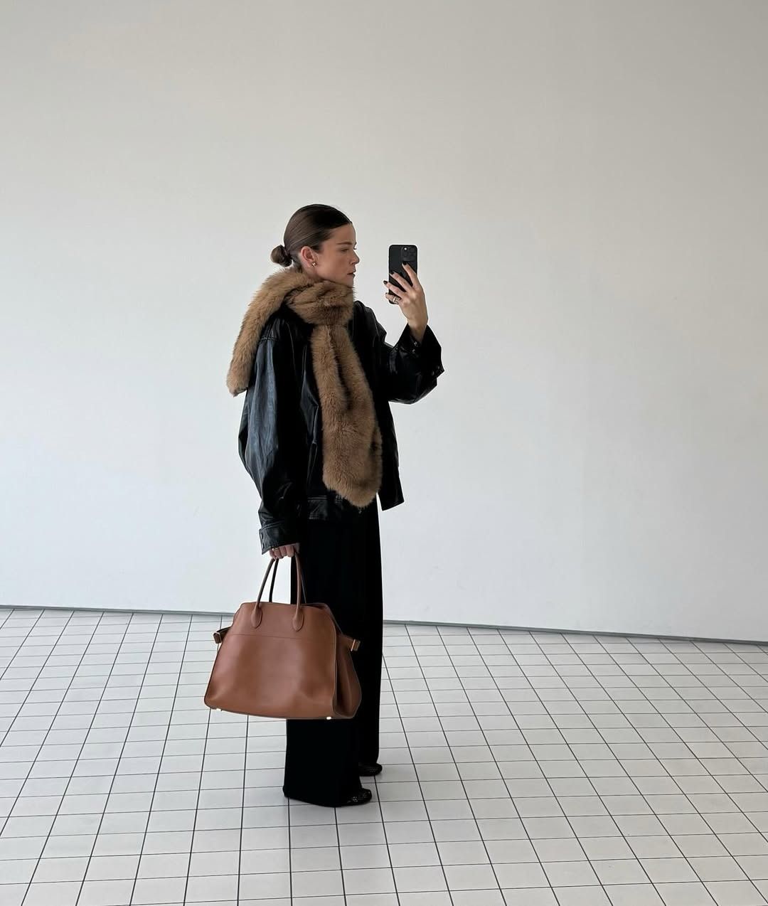 Rikke Krefting wears a black leather jacket, black trousers, a fur scarf, and a brown leather bag.