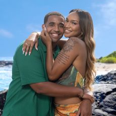 Sydney and Mikey from temptation island season 2 embrace one another smiling on a rocky beach in a promotional image for the show