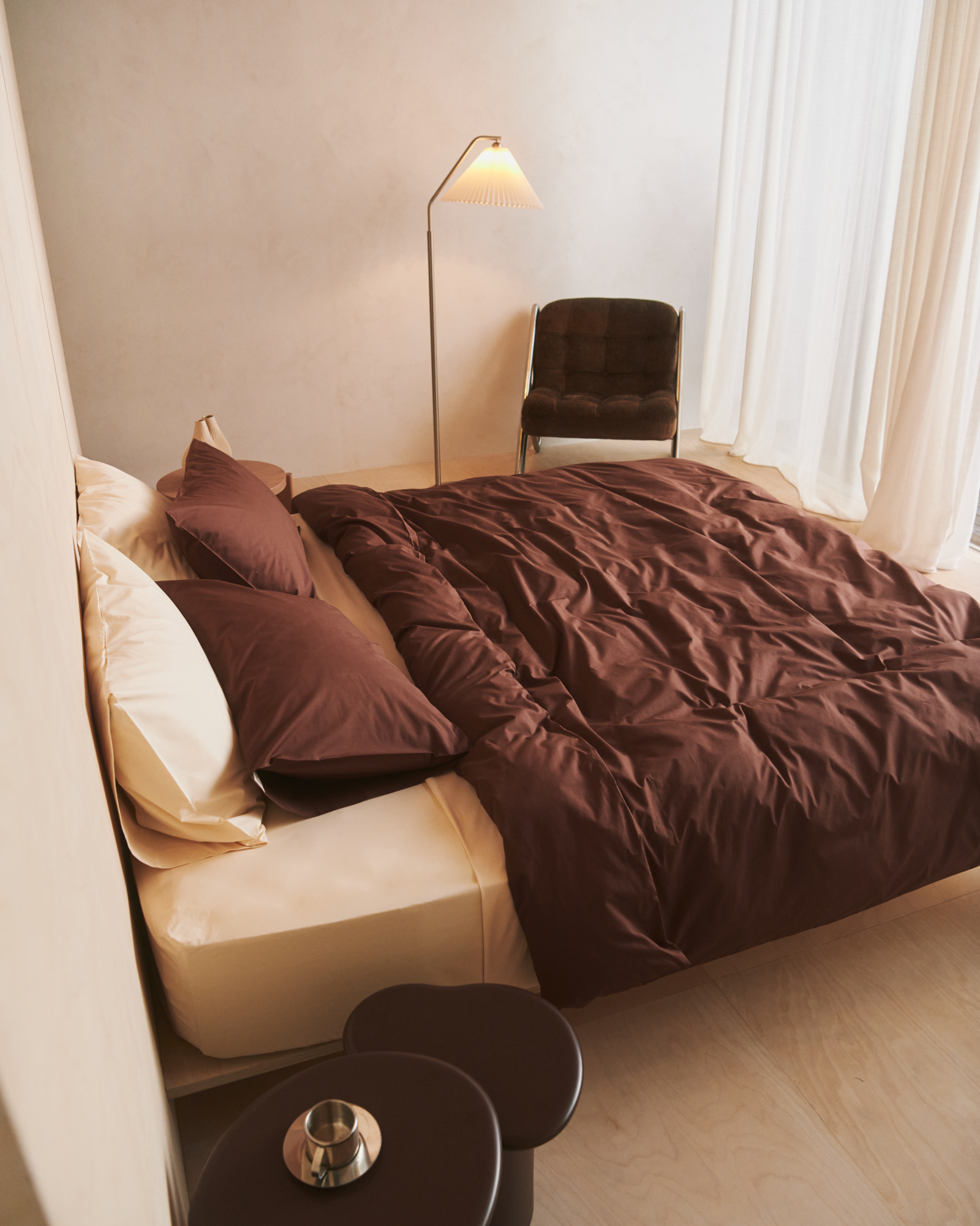 Dark brown duvet and pillows on top of warm beige fitted sheet and shams in neutral room