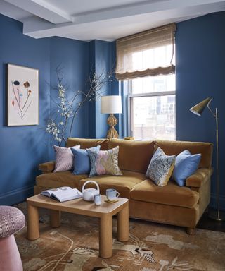 A family room with deep blue walls and a cognac brown velvet sofa
