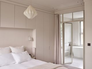 minimalist bedroom with japandi elements, silk pendant light hanging over bed, alcove bed with built-in storage around it, and glass doors covered by a curtain leading into an adjoining bathroom