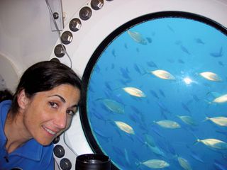 NASA astronaut Nicole Stott poses for a picture beside a habitat window during her 2006 stay inside the Aquarius Underwater Laboratory off the coast of Key Largo, Florida. Stott was a member of the ninth NASA Extreme Environment Mission Operations (NEEMO) mission.