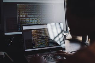 Programmer writing code on a laptop and second larger display