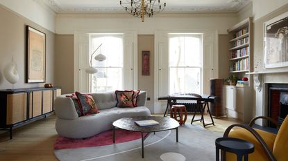 modern living room with antique furniture, curved sofa, round rug, timber coffee table, original fireplace, and chandelier