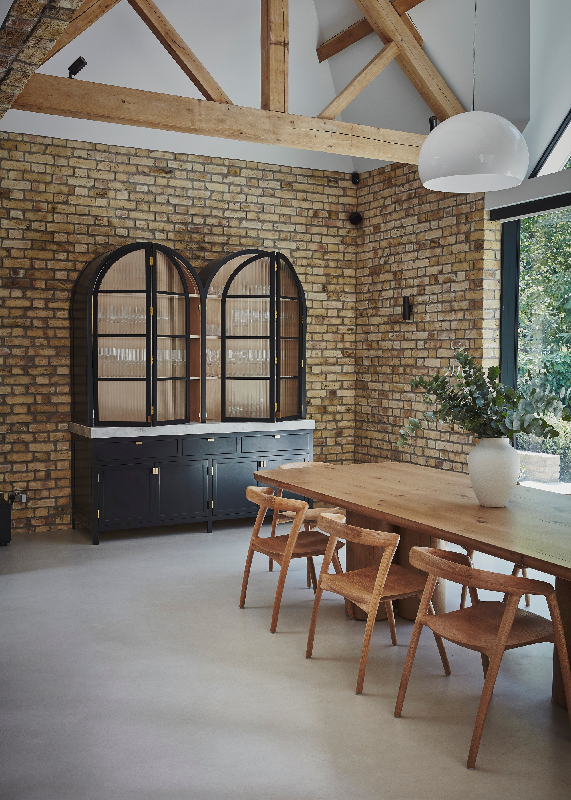 a large barn conversion dining room with wooden beams and a brick wall, with a wooden dining table and a freestanding cabinet