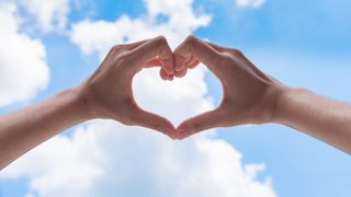 person making heart shape with hands with cloudy sky in the background