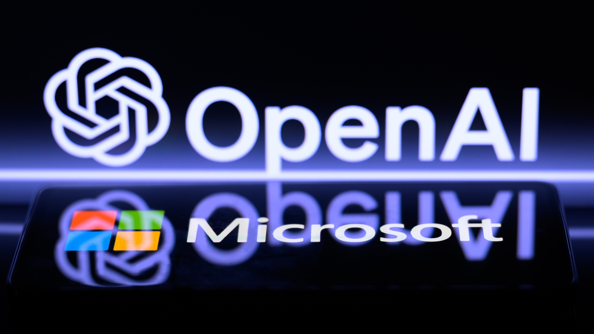 The Microsoft logo is being displayed on a smart phone, with the OpenAI logo visible on the screen in the background.