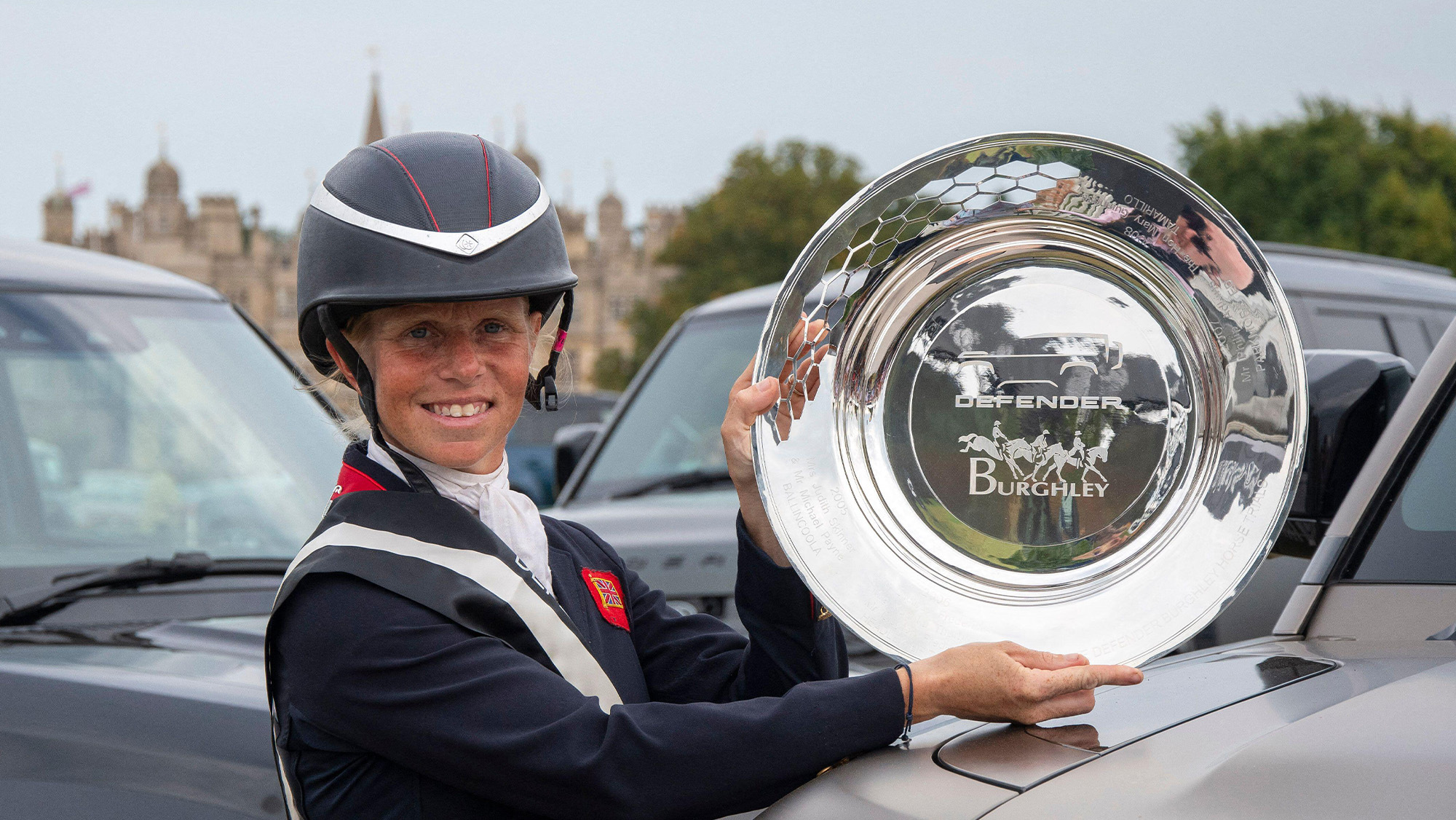 Close up of Ros Canter holding the Burghley Horse Trials trophy with Burghley House in the background