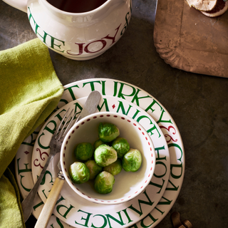 Bowl of brussel sprouts stacked on two plates, a gravy jug and pale green napkin