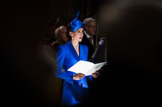 Kate Middleton wears a royal blue outfit with a matching hat and sings