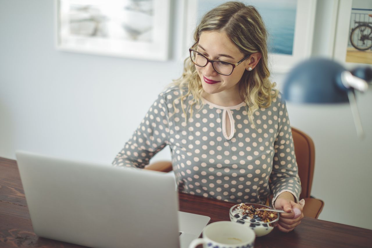 Woman researching stocks while eating a bowl of granola.