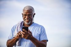 An older, active man smiling at his screen with earphones in. Demonstrating screen time for older adults.