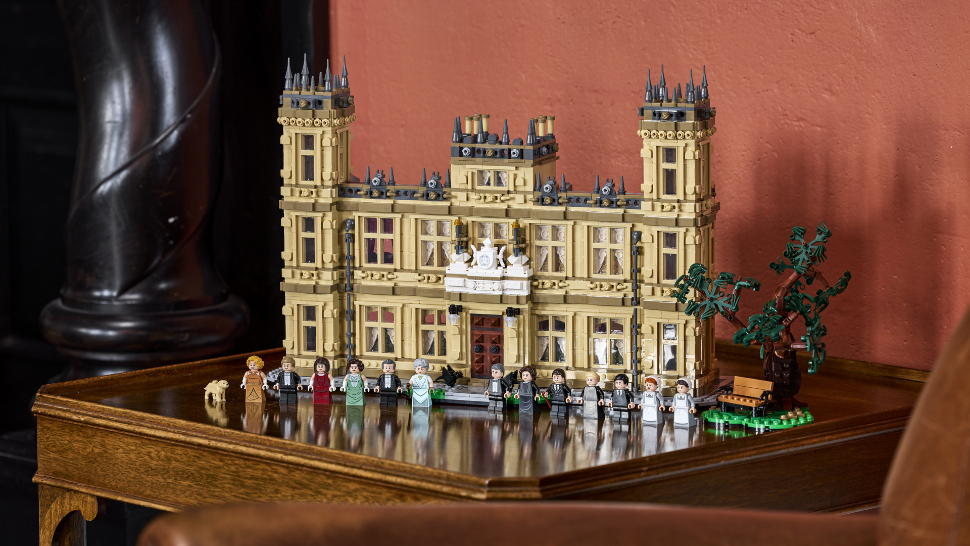 Lego Downton Abbey set and minifigures laid out on a glossy wooden sidetable, against a pink wall