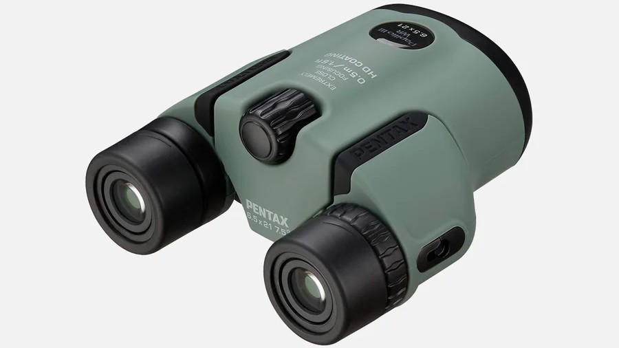 A pair of compact Pentax Papilio III 6.5x21 WR binoculars in a sage green color is shown at an angle on a white background.