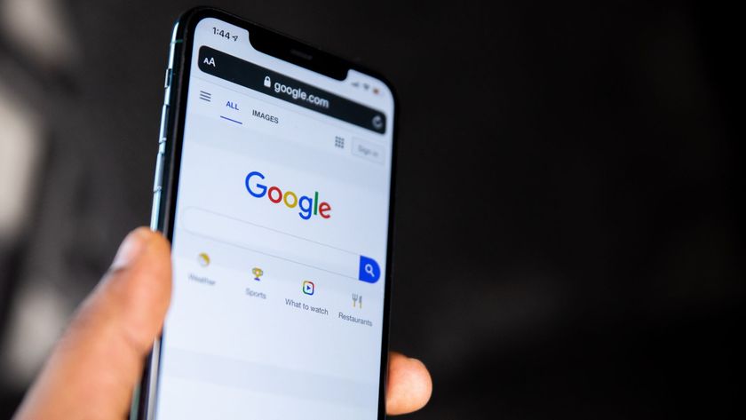 A person holding an iPhone close to the camera with the Google search homepage displayed onscreen