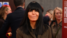 Image of Claudia Winkleman smiling at the camera with black straight hair with fringe wearing brown houndstooth blazer