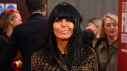 Image of Claudia Winkleman smiling at the camera with black straight hair with fringe wearing brown houndstooth blazer
