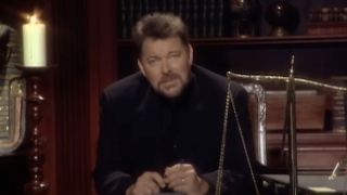 Jonathan Frakes sitting behind desk near a candle and scale, hosting Beyond Belief: Fact or Fiction
