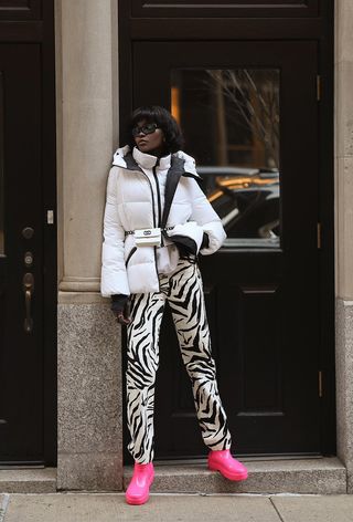 a roundup of the best puffer jackets shown in a photo of a woman wearing a white puffer coat with zebra print pants and pink rain ankle boots