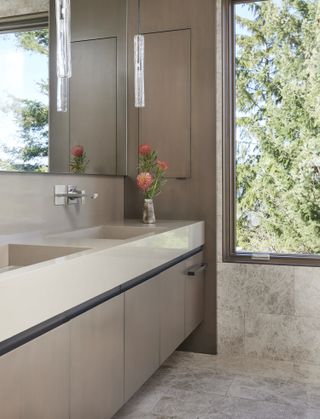 A beige marble bathroom with a vase of red flowers on the counter