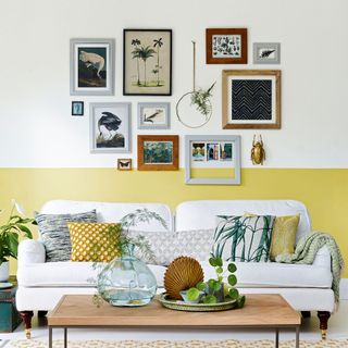 Living room with wall painted half yellow and white with gallery wall area above white sofa and coffee table
